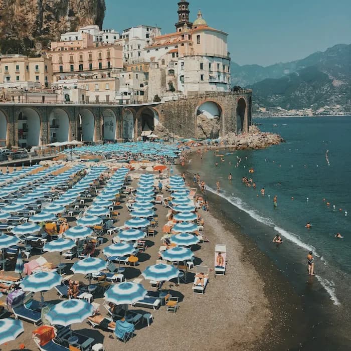 Striped parasols on a beach below the cliffside town of Atrani on the Amalfi Coast